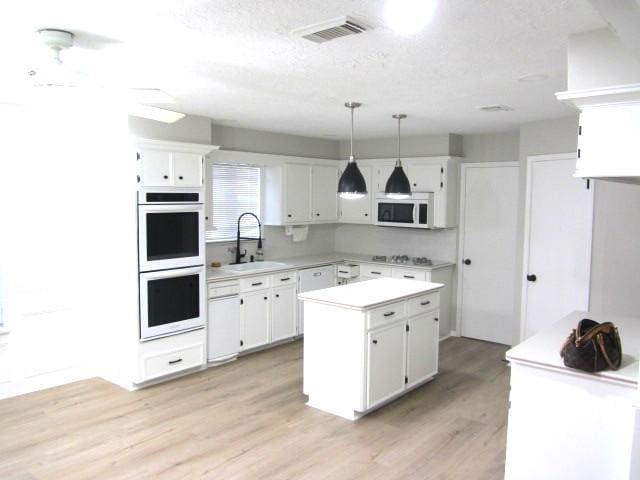 kitchen with light wood finished floors, visible vents, light countertops, white appliances, and a sink