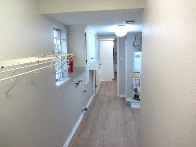 corridor with gas water heater, baseboards, and light wood-style flooring