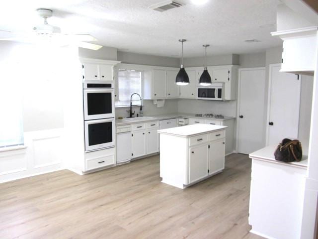 kitchen with a sink, a center island, white cabinetry, white appliances, and light countertops