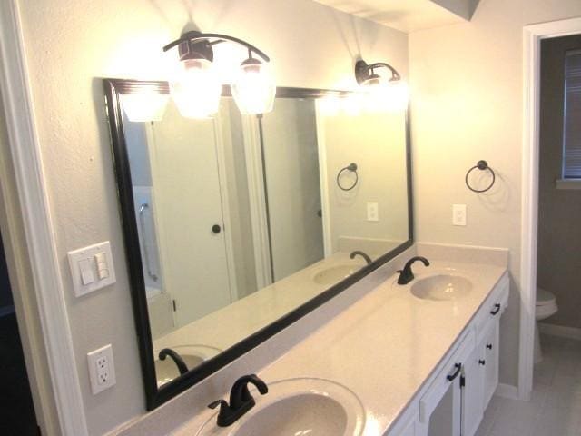 full bathroom with double vanity, toilet, and a sink