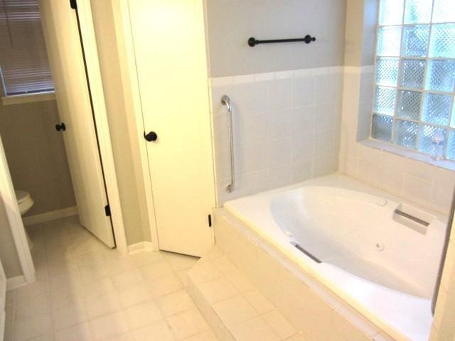 bathroom with a wealth of natural light, toilet, and a garden tub