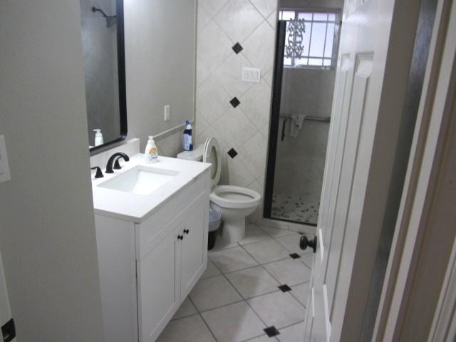 bathroom featuring toilet, tile walls, a shower stall, tile patterned flooring, and vanity