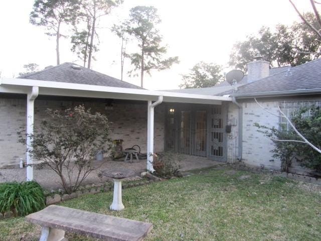 rear view of property with a lawn, a chimney, a patio, and roof with shingles