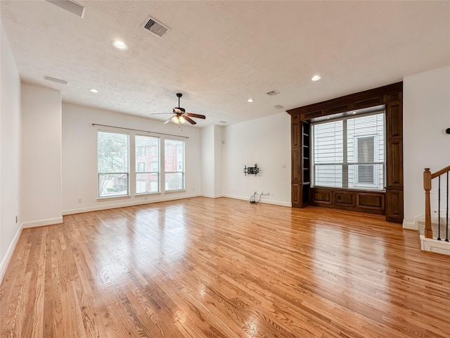 unfurnished living room featuring stairs, visible vents, light wood-type flooring, and ceiling fan