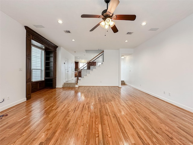 unfurnished living room featuring stairs, visible vents, light wood finished floors, and ceiling fan