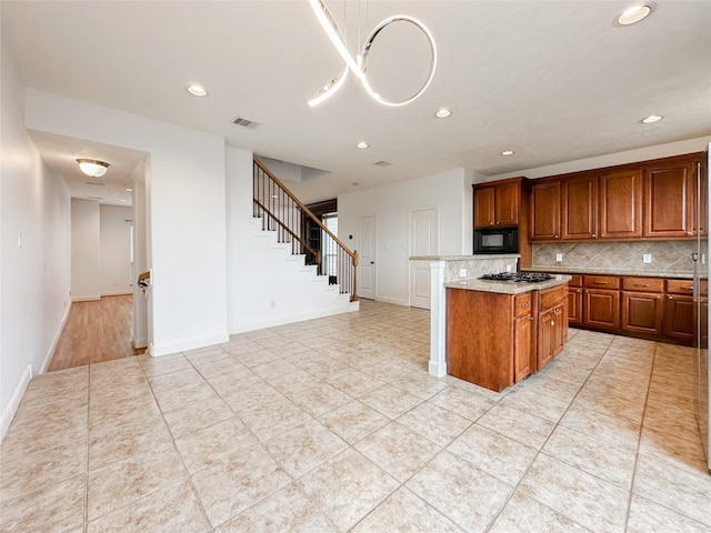 kitchen featuring visible vents, stainless steel gas cooktop, black microwave, brown cabinets, and backsplash