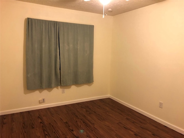 empty room featuring a textured ceiling, dark wood-type flooring, and baseboards