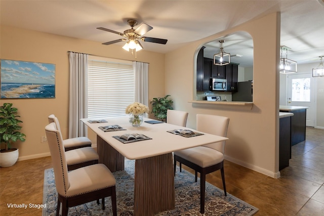 dining space with arched walkways, tile patterned floors, baseboards, and ceiling fan