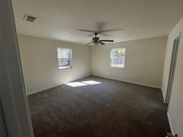 spare room with a ceiling fan, visible vents, dark carpet, and baseboards