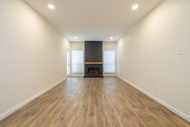 unfurnished living room featuring recessed lighting, a fireplace, baseboards, and light wood finished floors