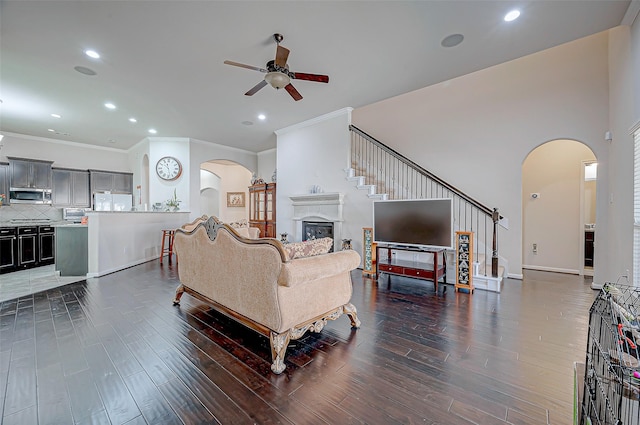 living room with arched walkways, ceiling fan, a glass covered fireplace, wood finished floors, and ornamental molding