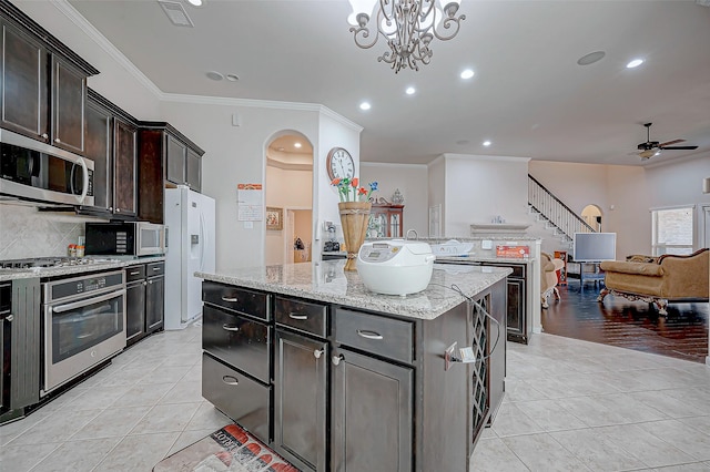 kitchen featuring appliances with stainless steel finishes, light tile patterned floors, a kitchen island, decorative backsplash, and ornamental molding