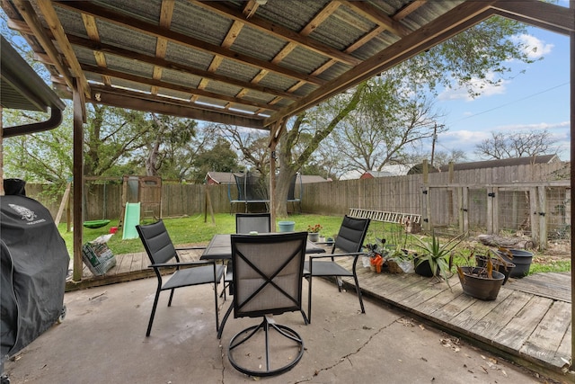 view of patio featuring outdoor dining area, a trampoline, area for grilling, and a fenced backyard