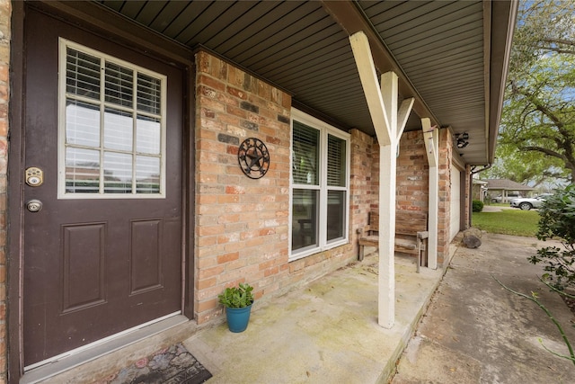 view of exterior entry with brick siding and a porch