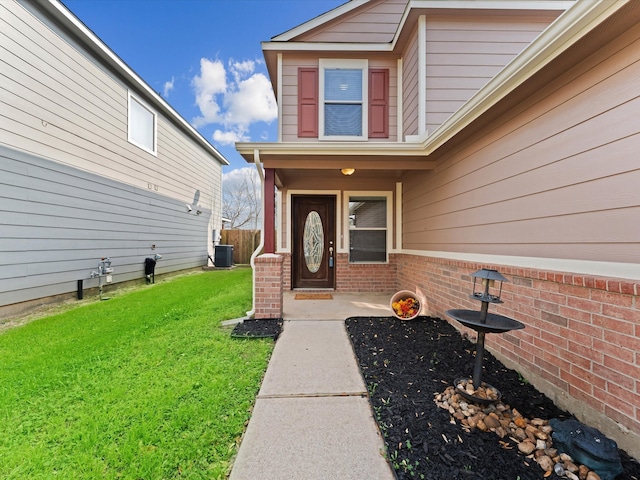 view of exterior entry featuring brick siding, central air condition unit, a yard, and fence