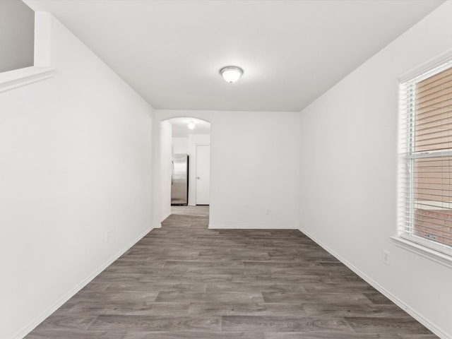 empty room with wood finished floors, arched walkways, and baseboards