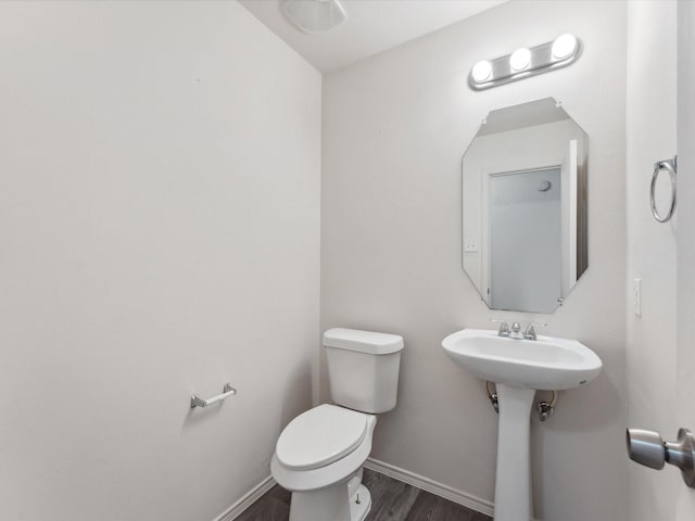 half bathroom with a sink, toilet, baseboards, and wood finished floors