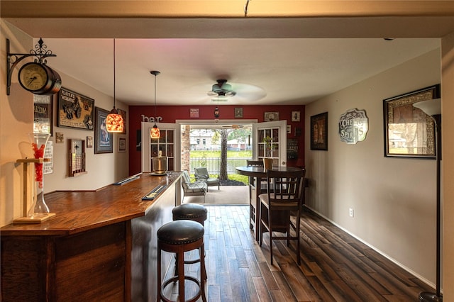 bar featuring dark wood-type flooring, a ceiling fan, baseboards, a dry bar, and hanging light fixtures