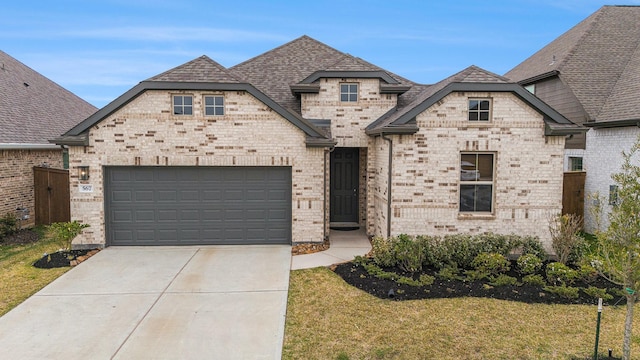 french provincial home with a shingled roof, concrete driveway, an attached garage, a front yard, and brick siding