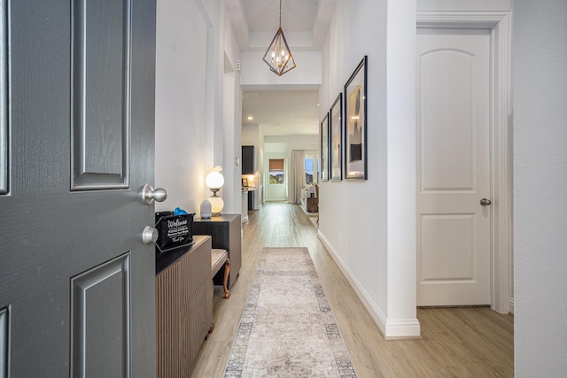 hallway featuring baseboards, an inviting chandelier, and light wood-style flooring