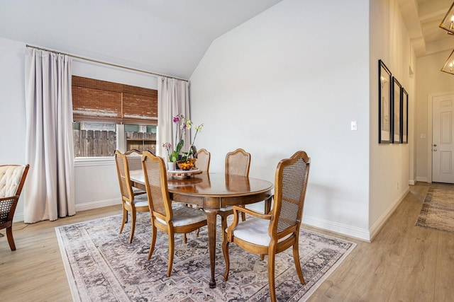 dining space featuring baseboards, light wood finished floors, and vaulted ceiling