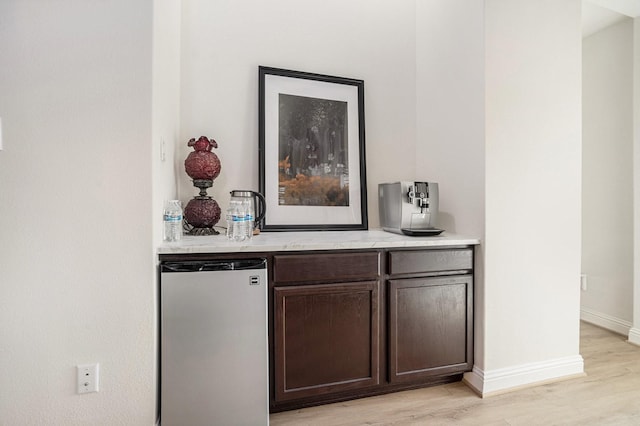 bar featuring a dry bar, light wood-style floors, baseboards, and freestanding refrigerator