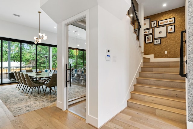 stairs featuring visible vents, hardwood / wood-style floors, an inviting chandelier, wallpapered walls, and an accent wall