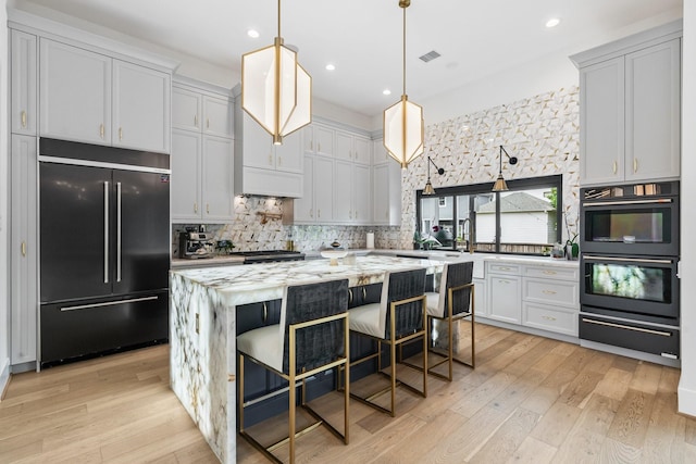 kitchen featuring visible vents, built in fridge, dobule oven black, a warming drawer, and light wood-type flooring