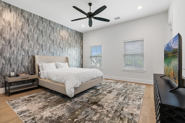 bedroom with wood finished floors, recessed lighting, wallpapered walls, baseboards, and an accent wall