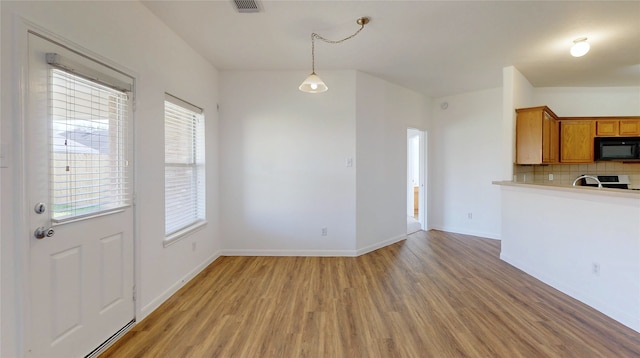 kitchen featuring baseboards, tasteful backsplash, black microwave, light wood-style floors, and brown cabinetry