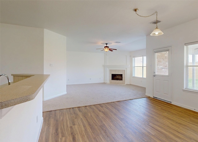 unfurnished living room featuring a tiled fireplace, a ceiling fan, baseboards, visible vents, and light wood-style floors