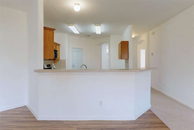 kitchen with decorative backsplash, range, arched walkways, brown cabinetry, and black microwave