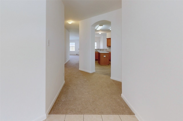 hall with light tile patterned floors, light carpet, baseboards, and arched walkways