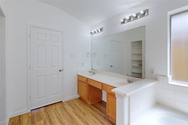 full bath with double vanity, lofted ceiling, a sink, and wood finished floors