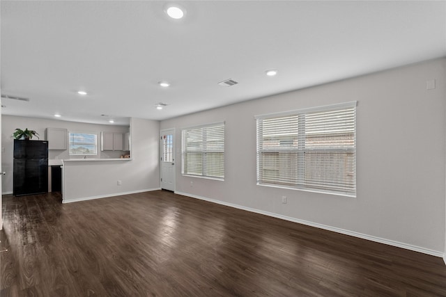 unfurnished living room with visible vents, plenty of natural light, and dark wood-type flooring