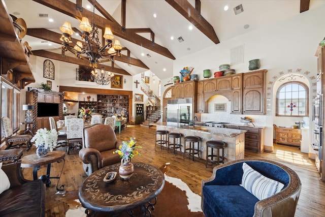 living room featuring a chandelier, light wood-style floors, visible vents, beamed ceiling, and high vaulted ceiling