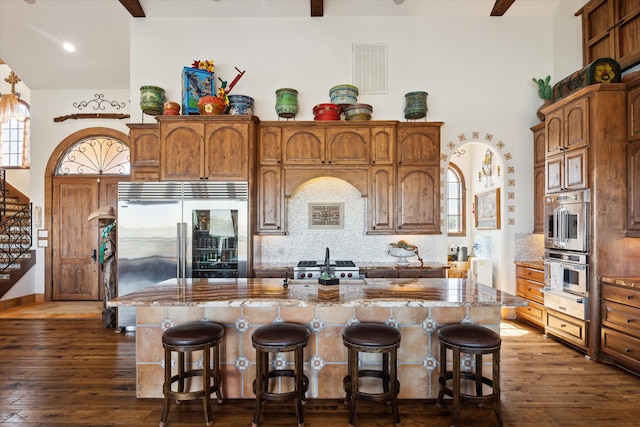 kitchen featuring tasteful backsplash, appliances with stainless steel finishes, dark wood-style floors, and a center island with sink
