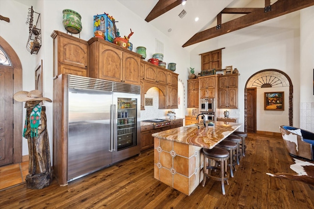 kitchen featuring high vaulted ceiling, beamed ceiling, light stone countertops, visible vents, and stainless steel appliances
