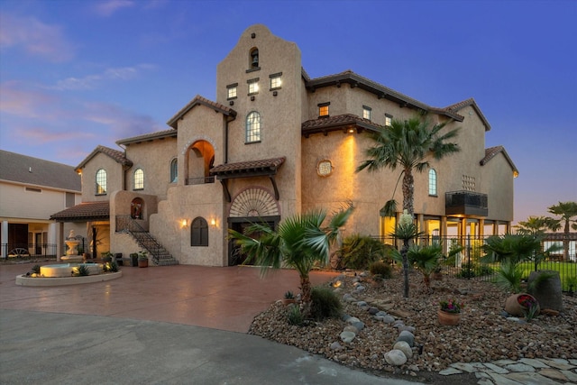 view of front of home with a tiled roof, curved driveway, fence, and stucco siding