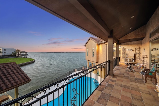 balcony at dusk featuring a water view and a patio