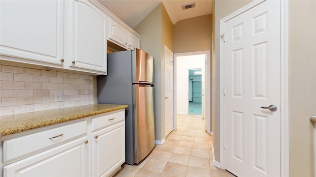 kitchen with visible vents, white cabinetry, freestanding refrigerator, light tile patterned flooring, and decorative backsplash