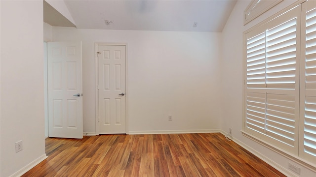 spare room featuring vaulted ceiling, baseboards, and wood finished floors