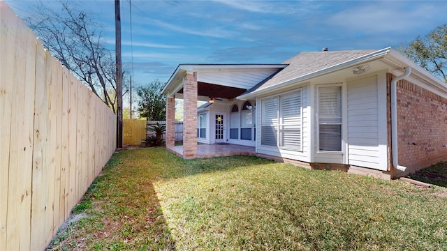 rear view of property featuring roof with shingles, a fenced backyard, a lawn, a patio area, and brick siding