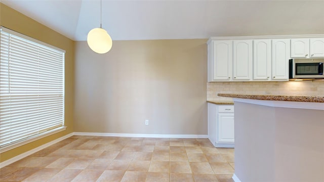 kitchen featuring pendant lighting, light stone counters, stainless steel microwave, white cabinetry, and decorative backsplash