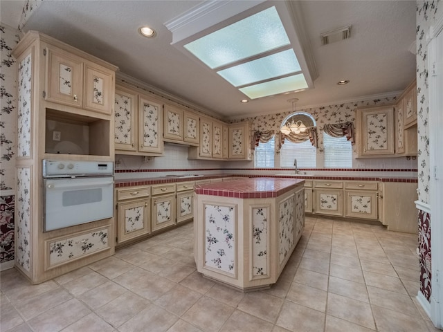 2402 Duhon Pl, Seabrook, TX 77586 - kitchen featuring white oven, cream cabinetry, a sink, a center island, and ornamental molding