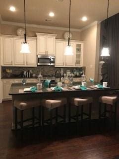 kitchen featuring stainless steel microwave, dark countertops, a kitchen breakfast bar, and decorative light fixtures