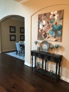 hallway featuring wood finished floors, baseboards, and arched walkways