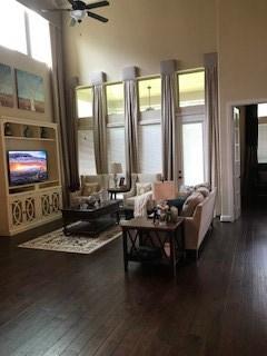living area featuring a towering ceiling, dark wood-type flooring, ceiling fan, and plenty of natural light