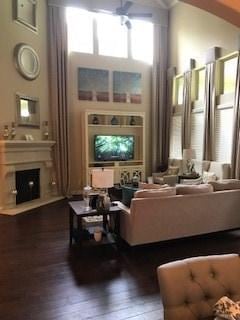living area with a fireplace, a towering ceiling, wood finished floors, and ceiling fan