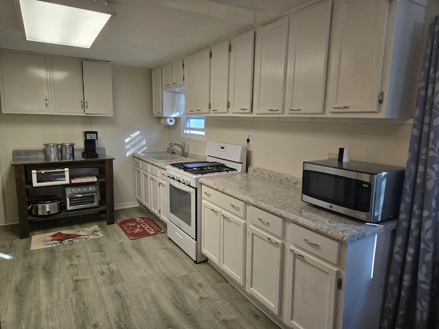 kitchen featuring white range with gas cooktop, a sink, light wood-style floors, white cabinetry, and stainless steel microwave